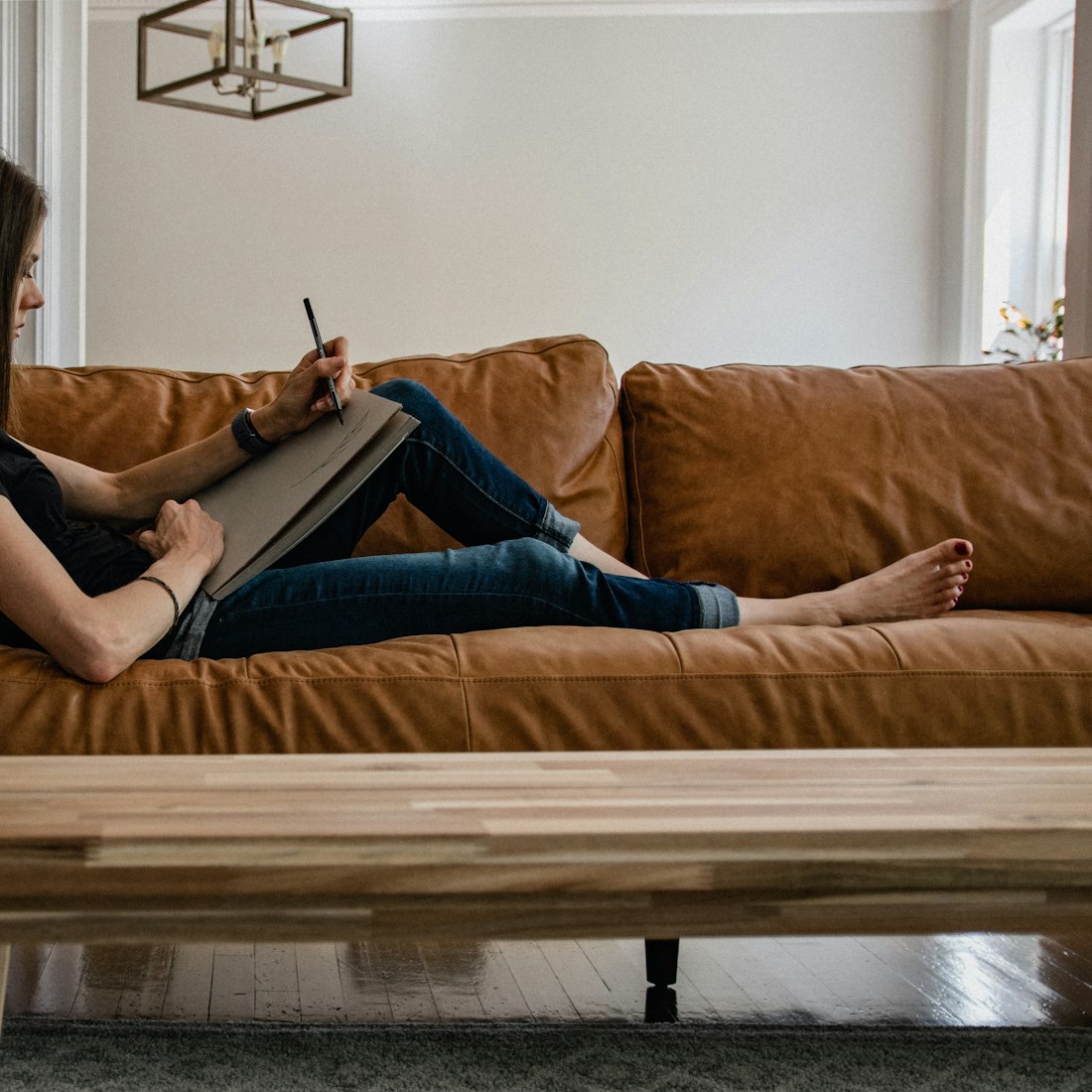A woman journaling calmly on a warm leather sofa at home